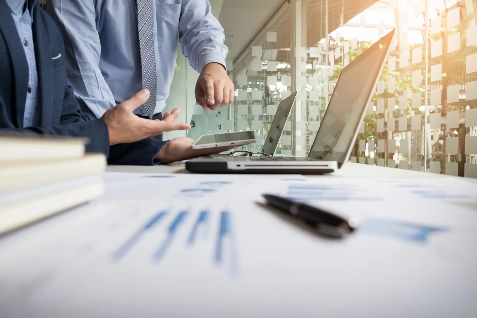 two professionals discussing over a laptop with charts and a pen on a desk