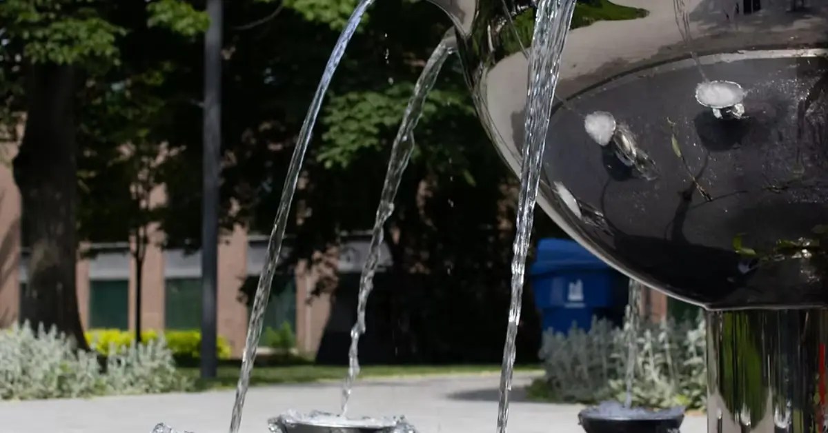 A-modern-shiny-silver-fountain-with-cascading-water-flows-from-its-bowl-into-smaller-basins-surrounded-by-greenery